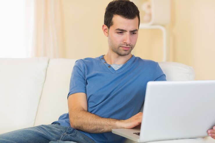 Foto casual pacífico hombre sentado en el sofá usando la computadora portátil