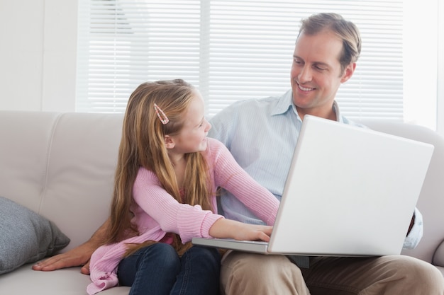 Casual padre e hija usando la computadora portátil en el sofá