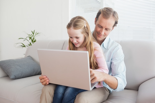 Casual padre e hija usando la computadora portátil en el sofá