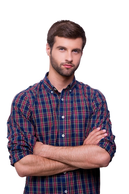 Casualmente guapo. Retrato de hombre joven guapo en camisa casual manteniendo los brazos cruzados y mirando a la cámara mientras está de pie aislado en blanco