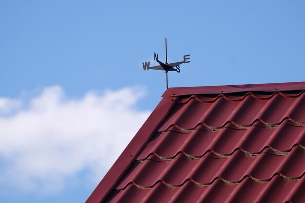 Cata-vento em um telhado de metal vermelho de uma casa sob um céu azul com nuvens brancas