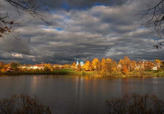 Catedral branca à distância, rodeada por árvores douradas de outono. A aldeia antes da tempestade. Cidade velha de Gatchina.