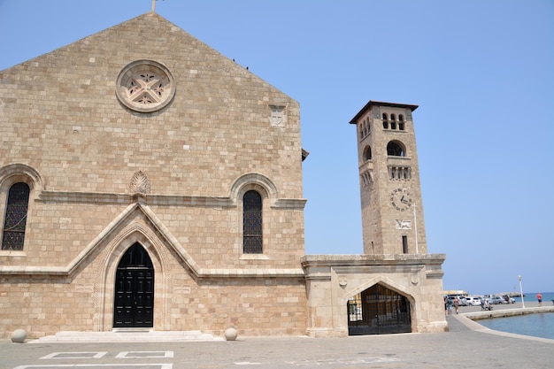catedral medieval con reloj de torre, ventanas y puertas arqueadas y plaza de piedra en la isla de Rodas