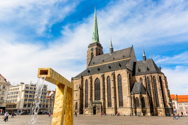 Catedral de San Bartolomé en la plaza principal de Plzen con una fuente en primer plano contra el cielo azul y las nubes día soleado.