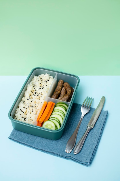 Catering-Lebensmittel, zubereitet in Vorratsbehältern mit Reiswürsten mit drei Fächern, Gemüse auf grünem Hintergrund, Mahlzeit mit gesunder, ausgewogener Ernährung, Lunchbox, verpackt, zum Mitnehmen, fertig verpackt