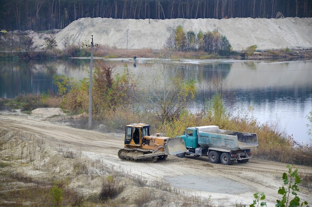 Caterpillar-Lader und Muldenkipper arbeiten im Tagebau-Steinbruch Schwere Maschinen im Tagebau am Fluss Dozer und LKW bei Grabarbeiten