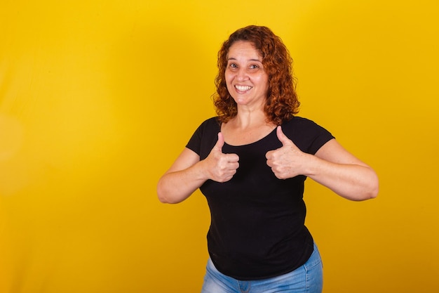 Caucasiana brasileira latino-americana de cabelo encaracolado com fundo amarelo polegar para cima aprovação afirmativa positiva ok confirmação correta