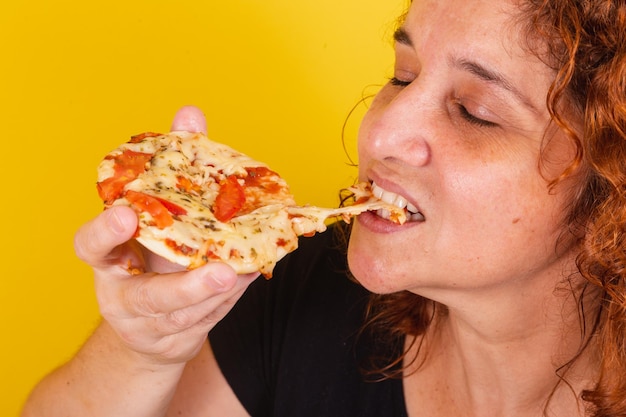 Foto caucasiana brasileira latino-americana de cabelo encaracolado de fundo amarelo comendo mini pizza comendo pizza comendo margarita pizza de queijo esticando delicioso