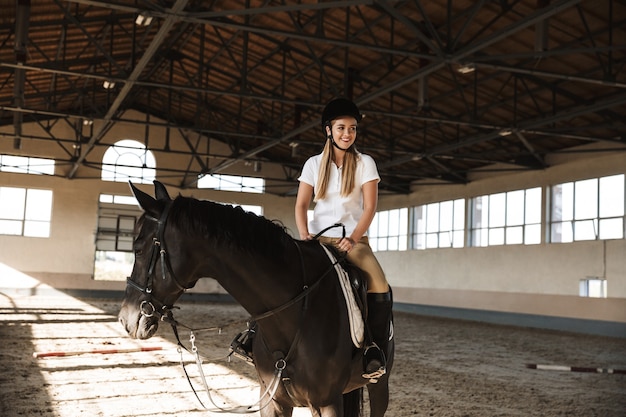 caucasiana jovem loira linda mulher usando chapéu com cavalo na zona rural em curral na área de treinamento.