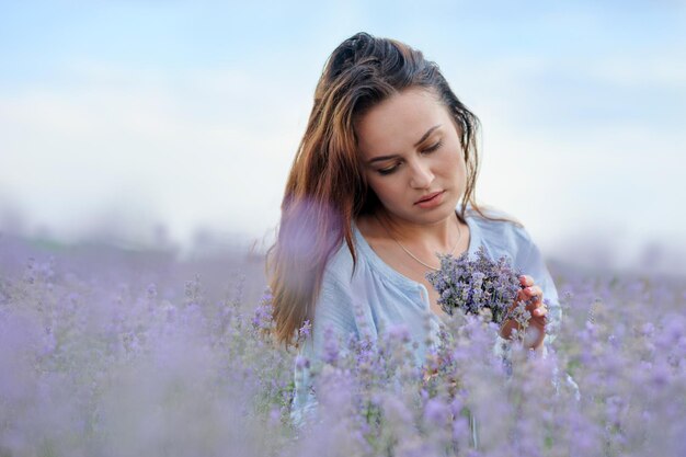 Caucasiana jovem sonhadora segurando um buquê de flores campo de lavanda no verão