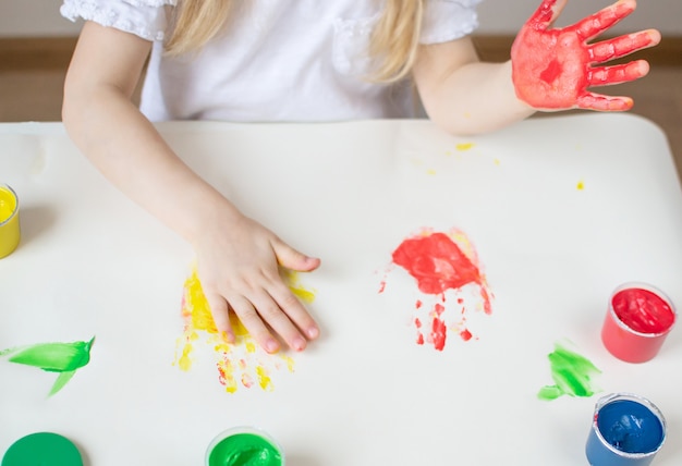 Caucasiana menina pintura com mãos coloridas pinta em casa educação infantil, preparando-se para o desenvolvimento da escola pré-escolar jogo para crianças