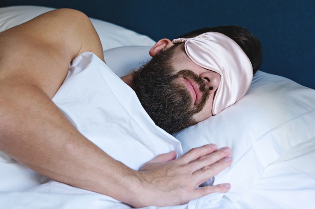 Caucasiano homem barbudo na máscara dormindo na cama
