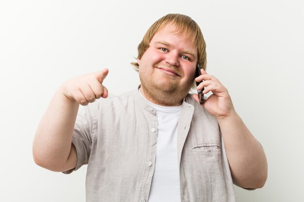 Caucasiano, mais tamanho homem telefonando por sorrisos alegres de telefone apontando para a frente.