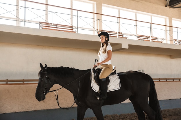 Caucásica joven rubia hermosa mujer con sombrero con caballo en campo en corral en área de entrenamiento.