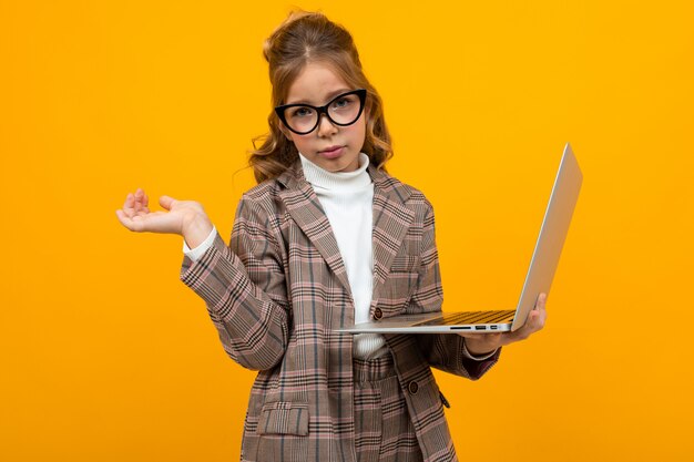 Caucásica niña con gafas en un traje de negocios con una computadora portátil en manos en amarillo