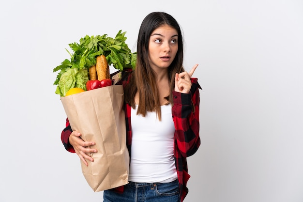 Caucásico joven con verduras aisladas en blanco pensando en una idea apuntando con el dedo hacia arriba