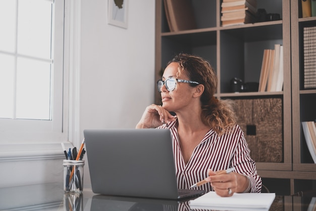 Caucásico reflexivo mirando la pantalla del portátil, reflexionando sobre el trabajo, empresaria independiente trabajando en un proyecto difícil. Persona de sexo femenino que se prepara en casa en la oficina interior.