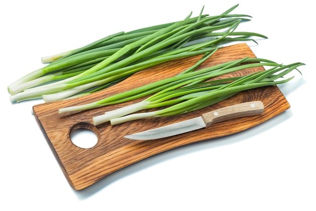 Caules de cebolinha verde na tábua de madeira e faca de cozinha isolada