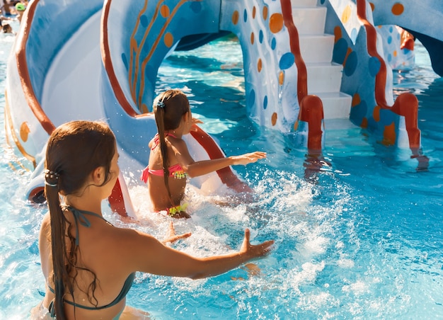 La cautelosa hermana mayor atrapa a su lindo pequeño que se desliza por el tobogán hasta la piscina.