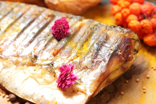 Cavala grelhada com bagas de batatas assadas e flores cor de rosa em papel pergaminho Conceito de comida saudável Closeup