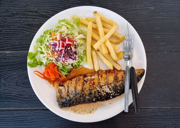 Cavala grelhada com salada e batata frita em fundo de madeira