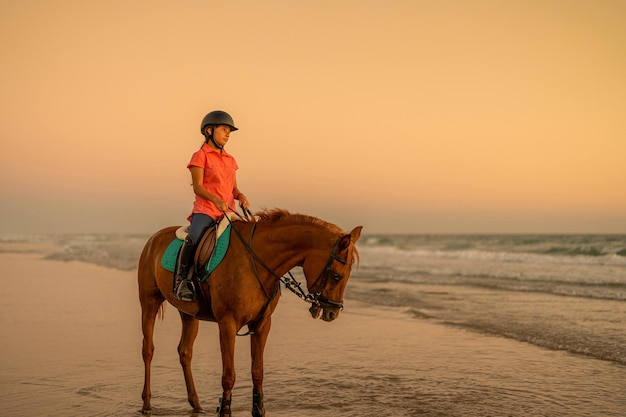 Cavaleiro de 15 anos em pé na praia montando seu cavalo