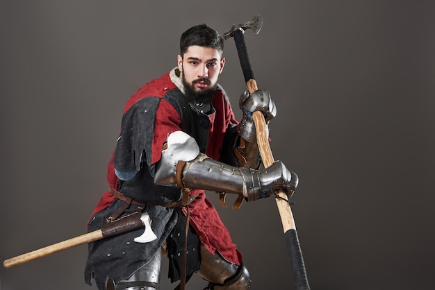 Cavaleiro medieval em cinza. retrato de guerreiro brutal rosto sujo com armadura de cota de malha vermelha e preta roupas e machado de batalha