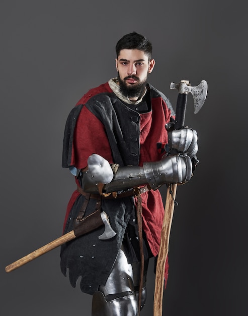 Cavaleiro medieval em cinza. retrato de guerreiro brutal rosto sujo com armadura de cota de malha vermelha e preta roupas e machado de batalha