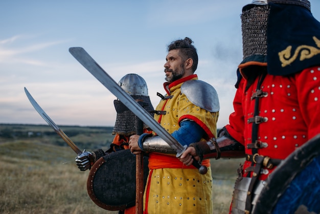 Cavaleiros medievais com espadas e machados em armaduras, grande lutador. antigos guerreiros com armaduras posando no campo