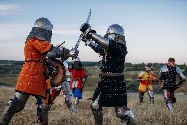 Cavaleiros medievais em armaduras e capacetes lutam com espadas. Antigos guerreiros armados posando no prado