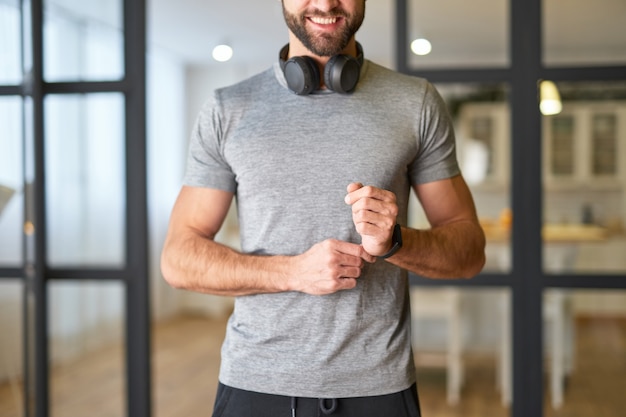 Cavalheiro alegre com fones de ouvido sem fio no pescoço, usando um relógio moderno e sorrindo