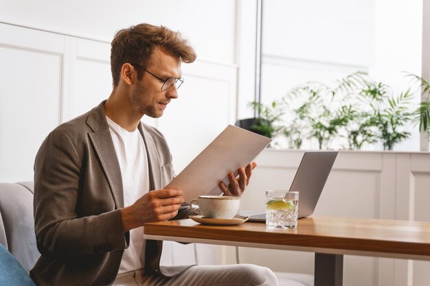 Cavalheiro estiloso escolhendo comida enquanto está sentado à mesa do café com um laptop moderno e uma xícara de café