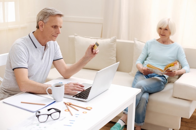 Cavalheiro inteligente e focado que emprega tecnologias modernas para administrar seu dinheiro e fazer pagamentos em casa