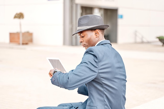 Cavalheiro usando tablet pc e olha para relógio de pulso na cidade jovem empresário de terno e chapéu trabalhando