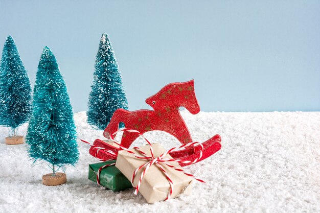 Cavalo de brinquedo retrô de Natal com pinheiros e caixas de presente na mesa de madeira coberta de neve