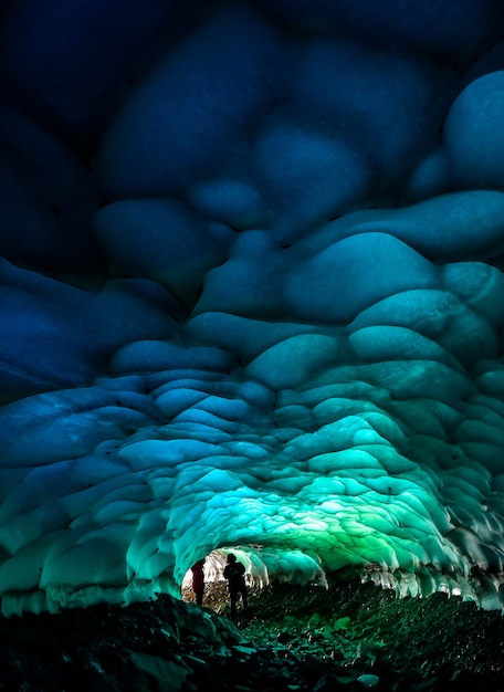 Foto caverna de gelo azul com silhuetas de pessoas dentro.