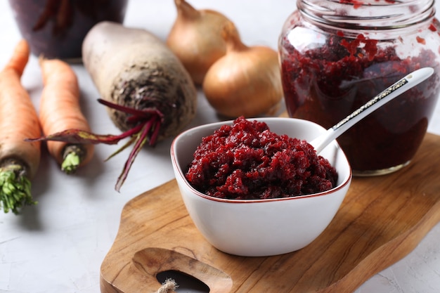 Caviar caseiro de beterraba e cenoura em uma tigela e frasco na placa de madeira e ingredientes frescos em uma superfície cinza claro, closeup