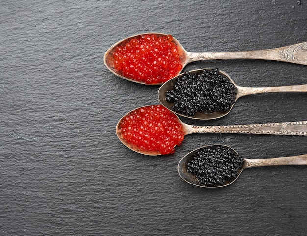 Caviar de peixe-paddlefish e caviar de salmão vermelho em uma colher, fundo preto, vista de cima