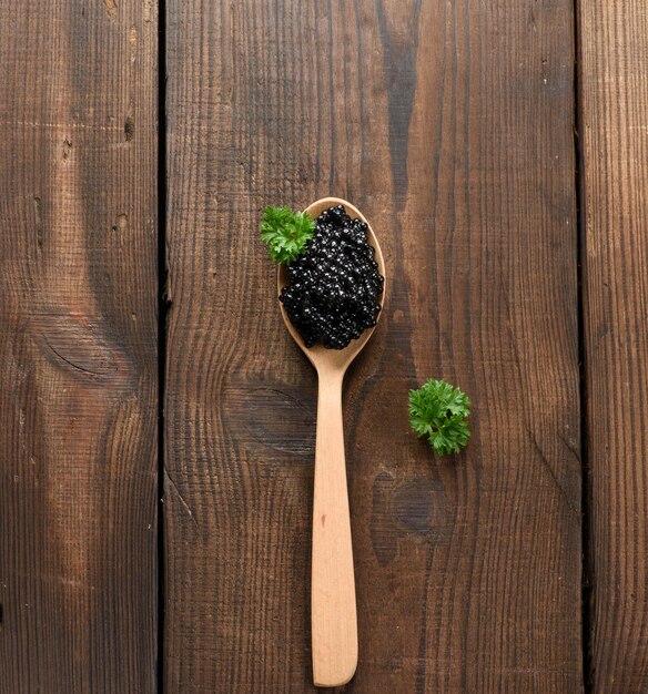 Caviar de peixe-pádel preto granulado fresco em colher de madeira marrom em um fundo preto