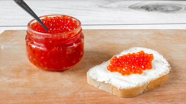 Caviar de salmão vermelho em uma jarra e em um sanduíche de manteiga.