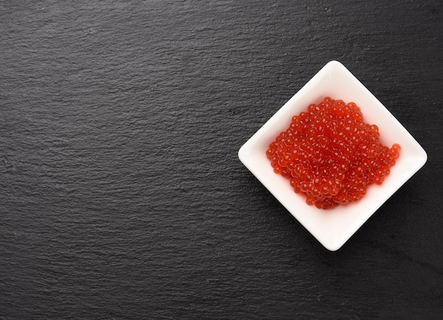 Foto caviar de salmão vermelho fresco em uma tigela de cerâmica branca sobre um fundo de pedra de ardósia preta