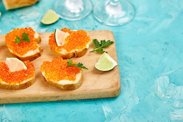 Caviar de salmão vermelho na tigela e sanduíches com tábua de madeira