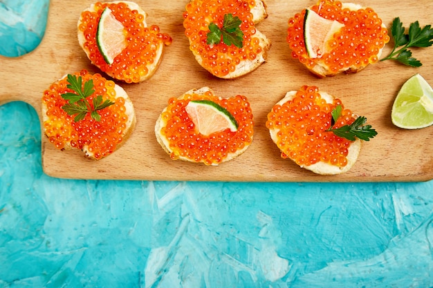 Caviar de salmão vermelho na tigela e sanduíches com tábua de madeira