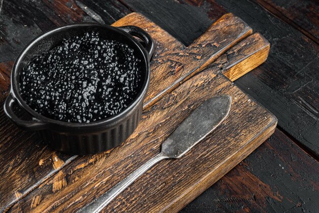Caviar de esturión negro en un tazón sobre un fondo antiguo de mesa de madera oscura