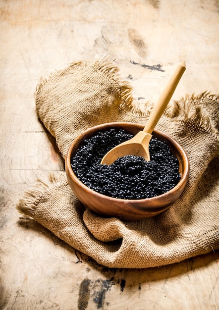 Caviar negro en un cuenco de madera sobre tela vieja. Sobre una mesa de madera.