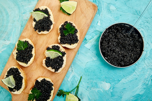 El caviar negro de esturión en un tazón de madera, sándwiches y champán sobre fondo blanco copia espacio.