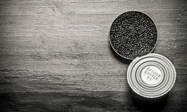 Caviar negro en un frasco. Sobre una mesa de madera negra. Espacio libre para texto. Vista superior