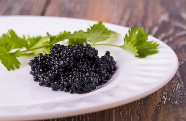 Caviar negro en un plato blanco con hierbas en mesa de madera