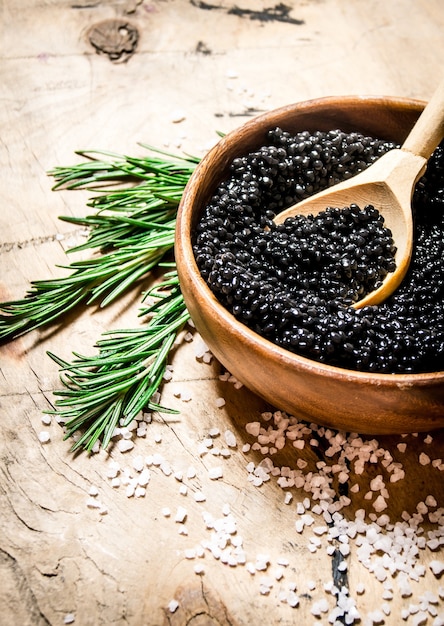 Caviar negro en taza con romero y sal. Sobre una mesa de madera.