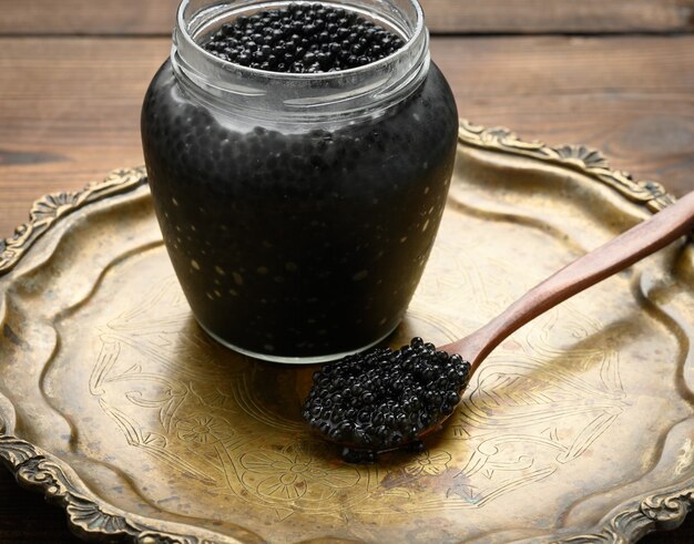 Caviar de pez espátula negro fresco en una cuchara de madera marrón y una lata llena de caviar en una mesa de madera, delicadeza